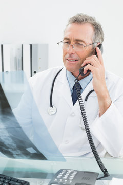 Doctor with xray picture while using telephone at office
