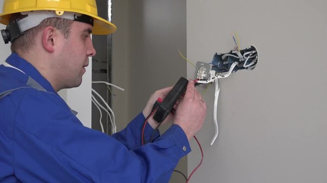 Man with helmet testing socket with voltmeter