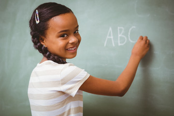 Cute little girl writing ABC on blackboard