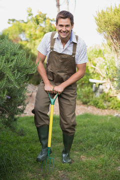 Happy man in dungarees raking the garden