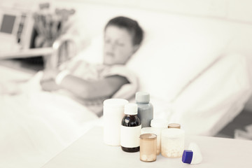 Fototapeta na wymiar Focus on medicines on table with sick boy in hospital bed