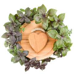 .Round cutting board with wooden heart in centre. Various sweet basil herb leaves edged.. Healthy food concept. Top view..