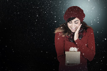Surprised brunette holding a gift against snow