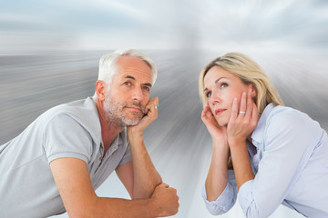 Thoughtful couple lying and looking up against room with large window looking on city