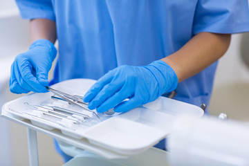 Mid section of nurse picking up dental tools from tray