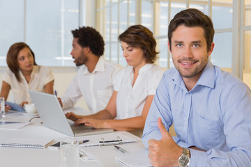 Smiling businessman gesturing thumbs up with colleagues in meeting