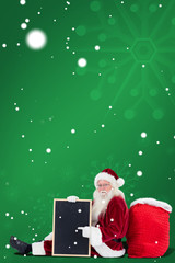Santa sits leaned on his bag with a board against green snowflake background