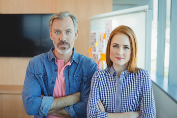 Portrait of male and female executives standing with arms crossed in conference room
