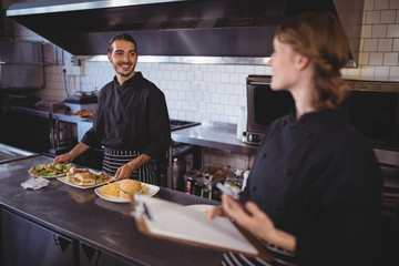 Young waiter preparing food while looking at waitress