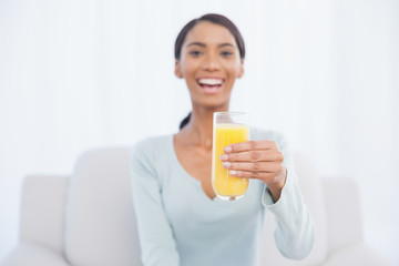 Fototapeta premium Smiling woman sitting on cosy sofa holding glass of orange juice