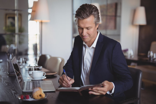 Smiling businessman writing on diary