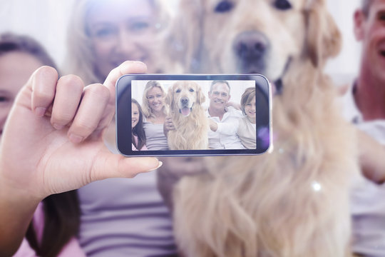 Hand holding smartphone showing against cute family relaxing together on the couch with their dog