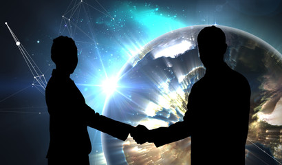 Smiling business people shaking hands while looking at the camera against earth seen from space