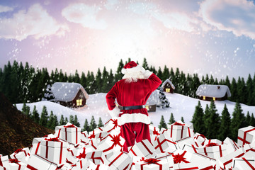Santa standing on pile of gifts against cute village in the snow