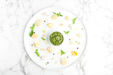 flat lay on marble table ingredients for green pesto sauce, garlic, pine nuts, Basil, Parmesan, black pepper, olive oil on round white plate