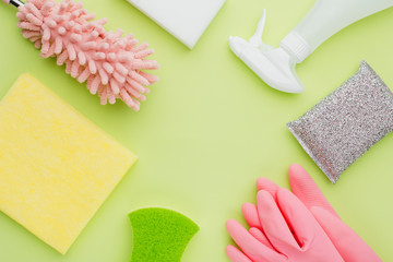 The concept of modern minimalistic cleaning and cleanliness, flat lay on a green background lime color lie pink rubber gloves and sprayer, sponge and duster and rags, place for text