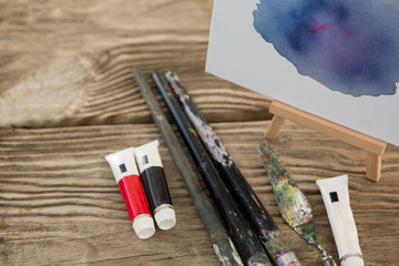 Watercolor paint, paint brushes and canvas on wooden surface