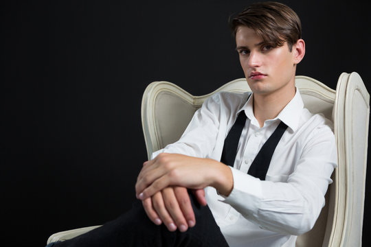 Androgynous man sitting on chair against black background - Powered by Adobe