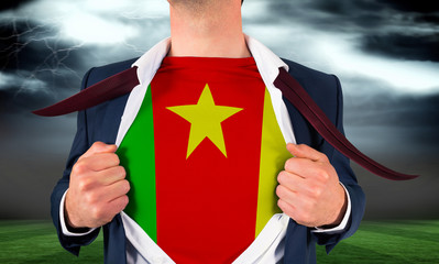 Businessman opening shirt to reveal cameroon flag against football pitch under stormy sky