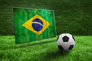 Black and white football on grass against brazil flag in grunge effect