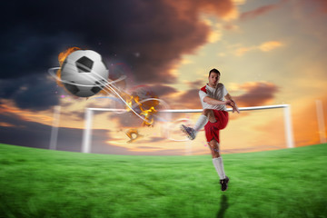Obraz na płótnie Canvas Football player in white kicking against football pitch under cloudy orange sky