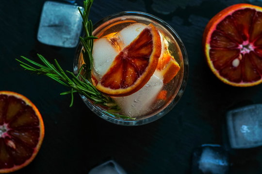 Detox water, refreshing cocktail with red blood orange, ice and rosemary on dark background.