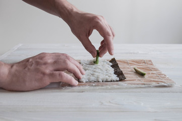 Process of making maki sushi. Cook chef hands preparing rolls with cheese, avocado, salmon and sesame seeds on wooden board 