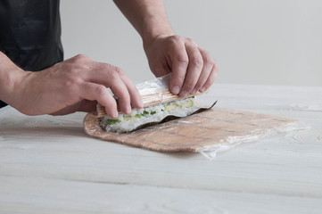 Process of making maki sushi. Cook chef hands preparing rolls with cheese, avocado, salmon and sesame seeds on wooden board 