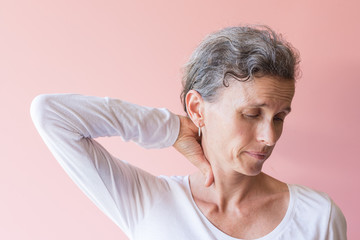 Middle aged woman with grey hair holding neck and grimacing with pain (selective focus)