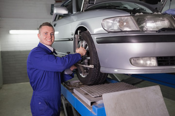Smiling mechanic standing while repairing a car wheel