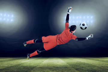Fit goal keeper jumping up against football pitch under spotlights
