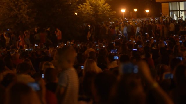 Hundreds of people making videos of fireworks on their smartphones on music festival. Concept: people, crowd, open air, summer, space, modern technology, happiness, rock concert, music festival.