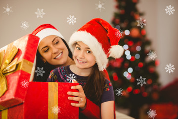 Fototapeta na wymiar Festive mother and daughter opening a christmas gift against snowflakes