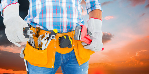 Midsection of handyman holding hand tools against orange and blue sky with clouds