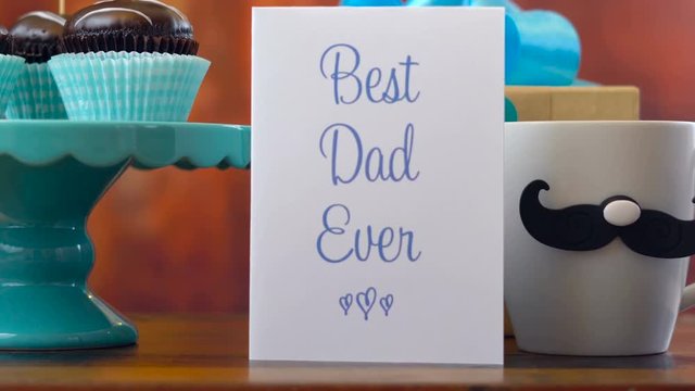 Happy Father's Day close up of woman arranging and setting up gift, cupcakes and card against rustic wood background.
