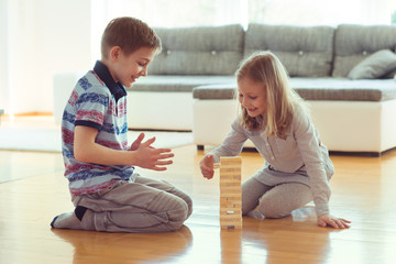 Two happy siblings playing a game with wooden blocks at home