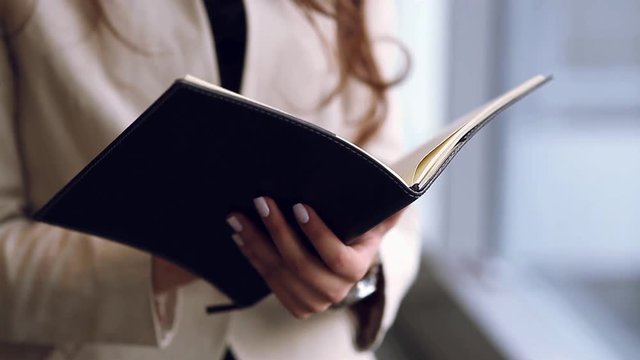 Cute business woman with Notepad in hand, opens the leafs and treats. Girl with a cute smile in the office, writes in the book standing. Planning for business ideas