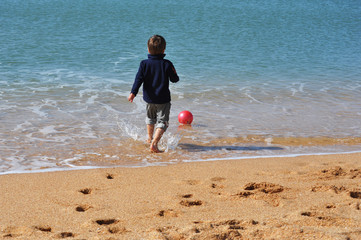 Мальчик босиком играет с мячом на пляже у моря