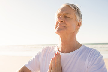 Active senior man with eyes closed in prayer position at beach