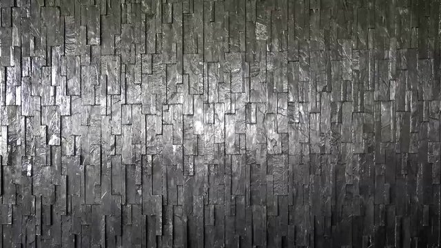 Artificial waterfall flows on a black stone wall.