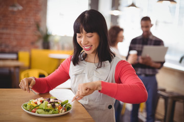 Happy young woman eating fresh healthy salad at coffee shop