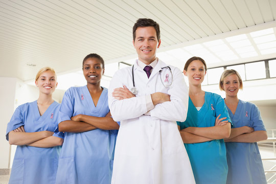 Smiling doctor and nurses with arms crossed wearing breast cancer awareness ribbon