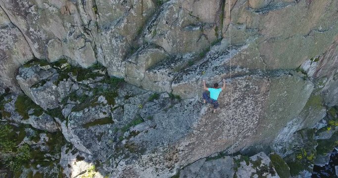 Climber is a mature man on a training climb on a rock among a granite canyon. Aerial view