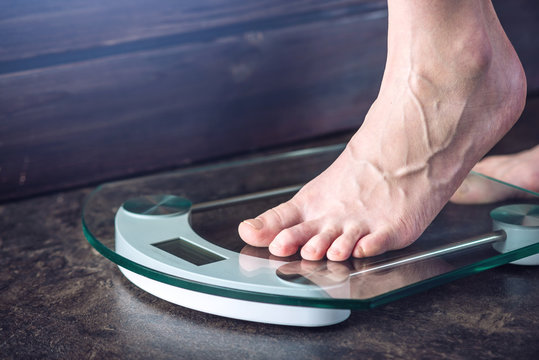 Female Feet Standing On Electronic Scales For Weight Control On Dark Background. Concept Of Sports Training, Diets