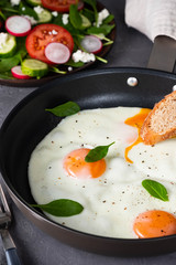 Fried eggs in a frying pan with  tomatoes and bread for breakfast on a black background.