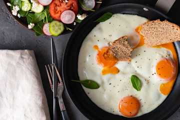 Fried eggs in a frying pan with  tomatoes and bread for breakfast on a black background.