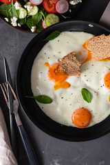 Fried eggs in a frying pan with  tomatoes and bread for breakfast on a black background.