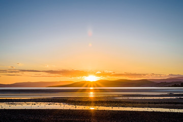 Hobart, Tasmania, Australia - Beautiful warm sunset sunrise over Mount Wellington with bright reflections in sea on low tide of the Tasman Sea ocean near South Arm Peninsula on summer holiday roadtrip