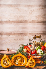 Pumpkin on kitchen table with cooking pot and ingredients at rustic wall background, front view. Healthy vegetarian  food and eating concept.  Autumn seasonal eating