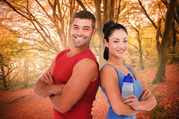 Fit man and woman smiling at camera together against peaceful autumn scene in forest